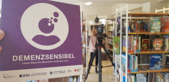 Die Fotos zeigen Impressionen vom Filmdreh in der Ernst-Abbe-Bücherei. Zu sehen ist ein Kameramann, der zwischen den Bücherregalen ein Interview führt.
