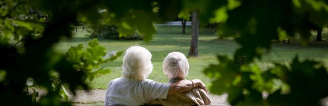 Zwei ältere Menschen sitzen auf einer Bank in der Natur