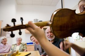Ein Musiker mit Geige spielt vor einer Gruppe älterer Menschen