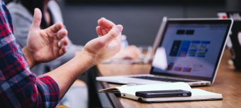 Beratungssituation, zwei Personen sitzen an einem Tisch mit Notizublöcken und Laptops